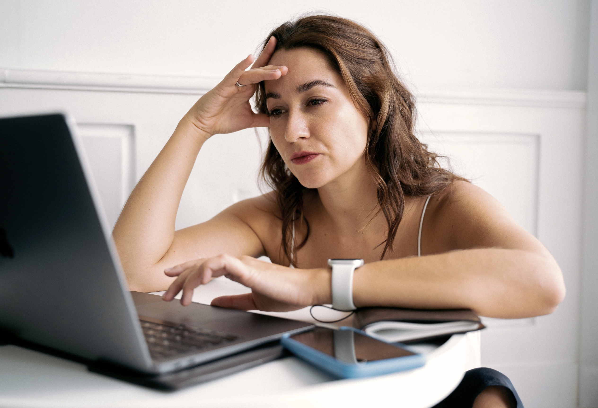Woman at a laptop with her hand on her forehead, feeling overwhelmed