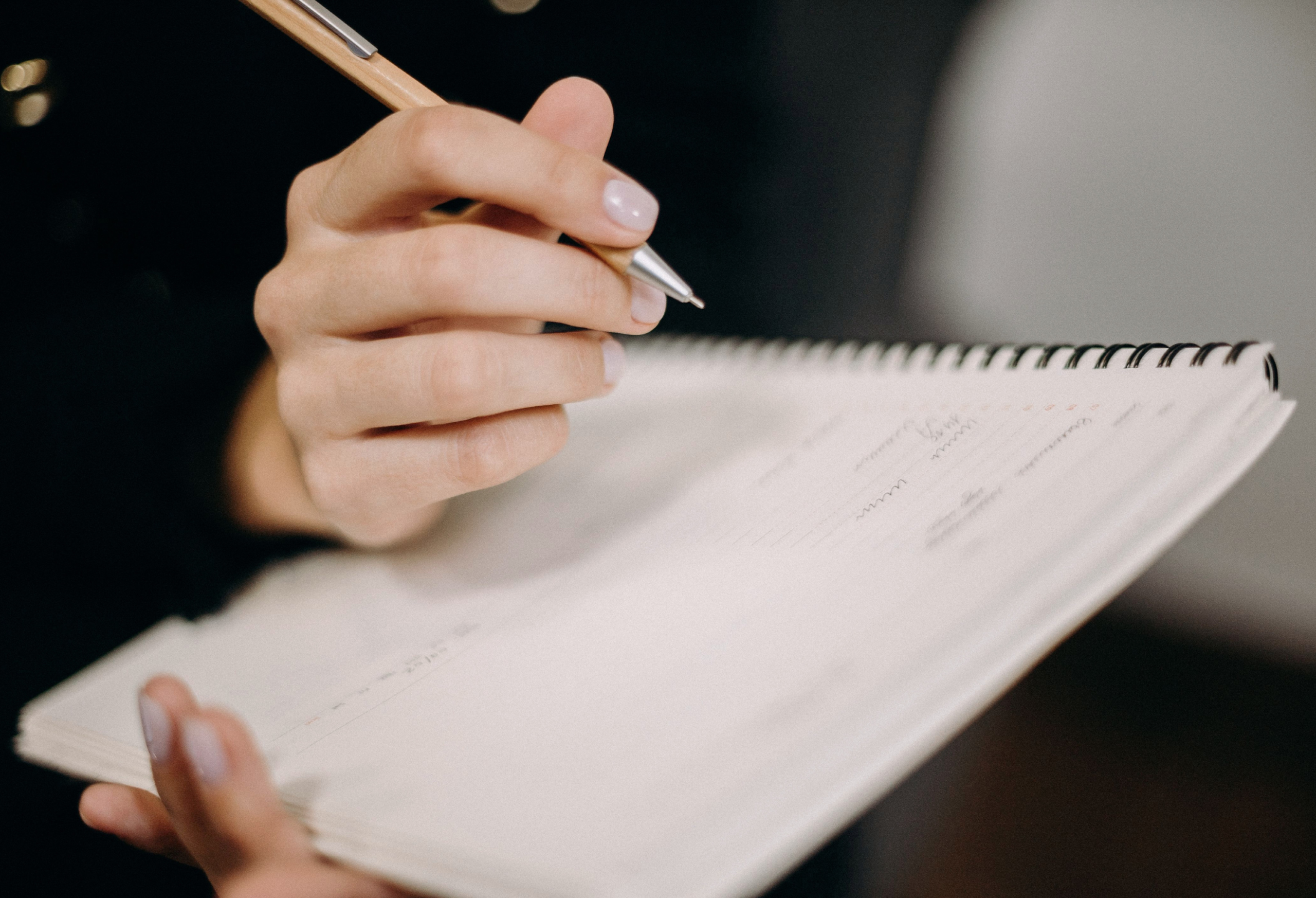 Close-up of a hand writing in a spiral notebook